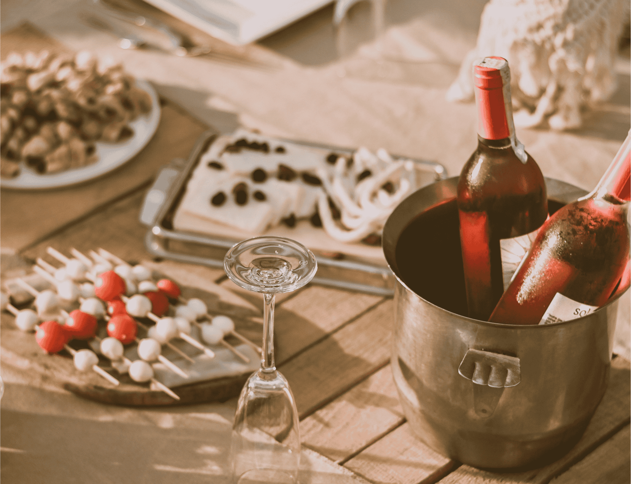 Chilled ros wine bottles in an ice bucket on a wooden table with skewered appetizers and cheese for a beachside picnic